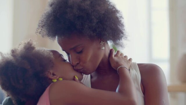 Closeup of loving mother and cute little daughter hugging and kissing. Beautiful African American woman showing affection holding and caressing her child. Static shot. Motherhood, happy family concept