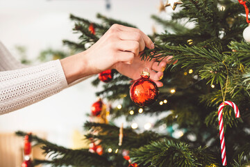 Woman hand holding a red ornament putting it on the Christmas tree