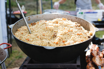 Defocus stirring the pilaf in a large bowl during cooking outdoors. National dish. Cooking of traditional pilaf in big cauldron, street food in outdoor. Festival. Out of focus