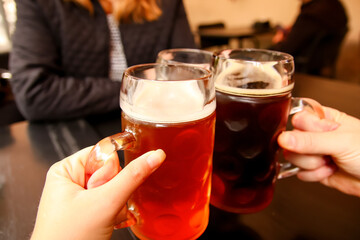 Defocus mug of light beer. Closeup of three hands clinking beer stein glasses. Company friends drinking beer in pub. Cheers. Out of focus