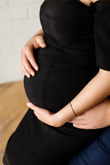 A pregnant woman and a loving husband hugs her stomach on a white background. The feeling of the baby's movement by a couple on the pregnant woman's stomach. Close-up.
