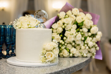 A light birthday cake decorated with white flowers on the background of the restaurant.