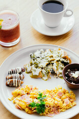 Mexican food, egg with ham, beans, chilaquiles, juice and cup of coffee.