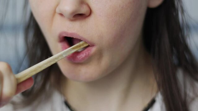 A young woman brushes her teeth with a brush made of bamboo wood. Biodegradable products concept. Zero waste concept.