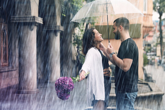 Young couple with umbrella enjoying time together under rain on city street, space for text