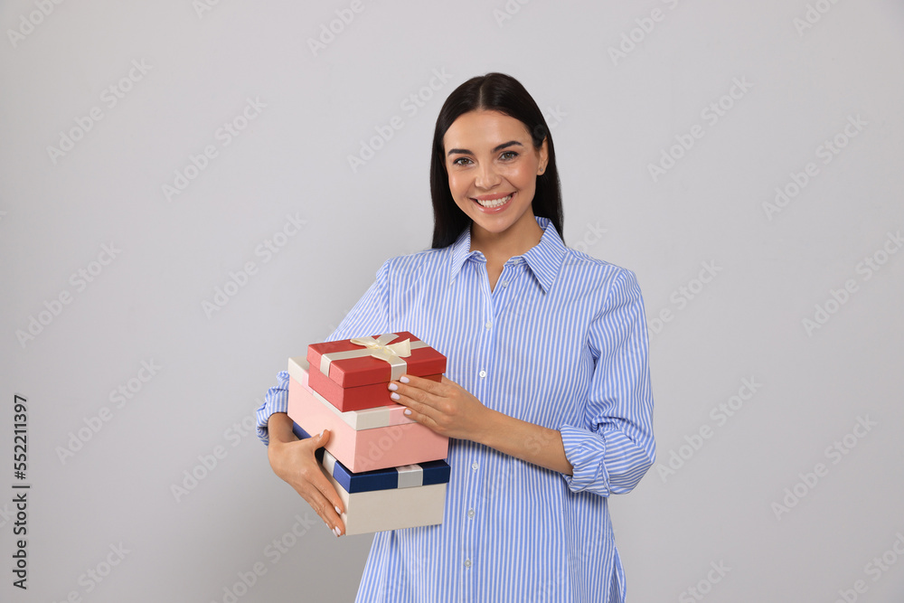 Canvas Prints Happy young woman holding gift boxes on light grey background