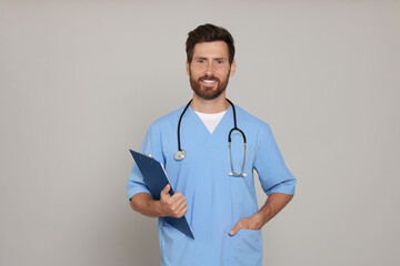 Happy doctor with stethoscope and clipboard on light grey background