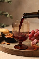 Pouring red wine into glass at wooden table, closeup
