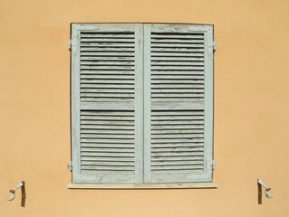 Window with closed wooden shutters on orange wall