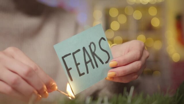 A woman burns a sheet with the word fears with a Christmas background. Video about mental problems during the war.