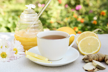 Cup of delicious tea with honey, lemon and ginger on white table outdoors