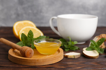 Bowl with honey for tea, lemon, mint and ginger on wooden table