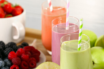 Glasses of different tasty smoothies and fresh ingredients on wooden tray, closeup