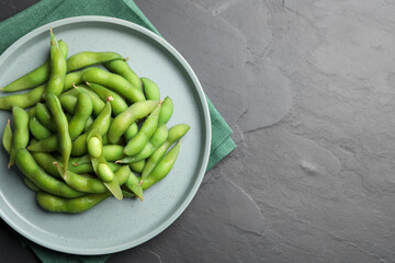 Plate of green edamame beans in pods on black table, top view. Space for text