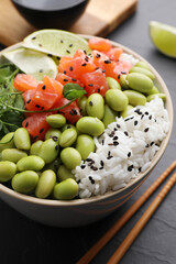 Delicious poke bowl with lime, fish and edamame beans on black table