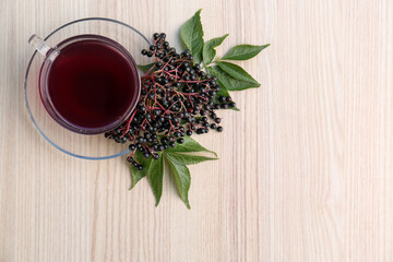 Glass cup of tasty elderberry tea and Sambucus berries on wooden table, top view. Space for text