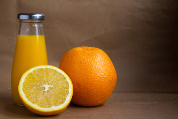 a bottle of orange juice and the fruit itself and a juicy half of an orange on a light brown background