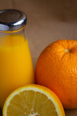 a bottle of orange juice with a shiny cap and the fruit itself and half an orange on a light brown blurred background - vertical photo