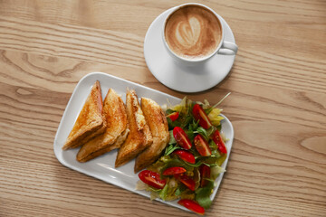 Plate of delicious toasts with salad and coffee cup on wooden table, flat lay