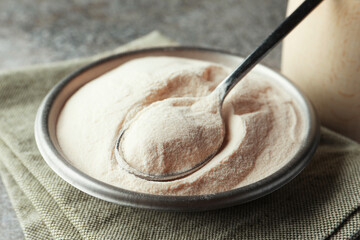 Bowl and spoon of agar-agar powder on grey table, closeup