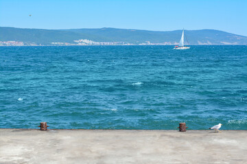 Beautiful seascape with concrete pier and sailboat on sunny day
