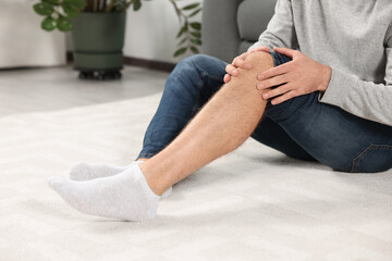 Man suffering from leg pain on white carpet at home, closeup