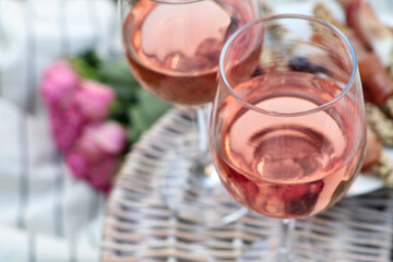 Glasses of delicious rose wine and food on picnic basket outdoors