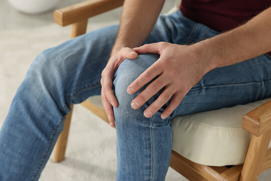 Man touching knee on soft armchair, closeup