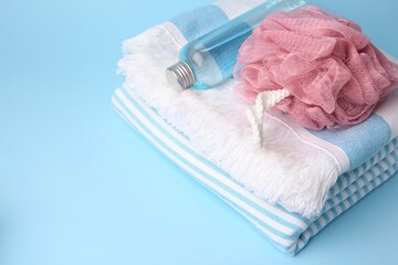 Obraz na płótnie Canvas Pink shower puff, bottle of cosmetic product and towel on light blue background, space for text