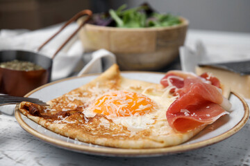 Delicious crepe with egg served on white wooden table, closeup. Breton galette
