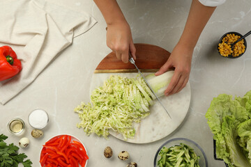 Woman cutting fresh Chinese cabbage at light grey table, top view