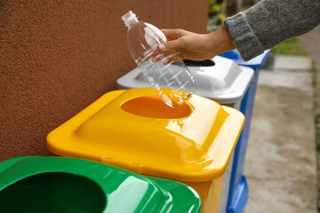 Woman throwing plastic bottle into recycling bin outdoors, closeup