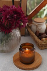 Beautiful pink chrysanthemum flowers, burning candle and sweet chocolate treats on light grey table