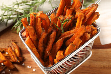 Frying basket with sweet potato fries and rosemary on wooden table, closeup