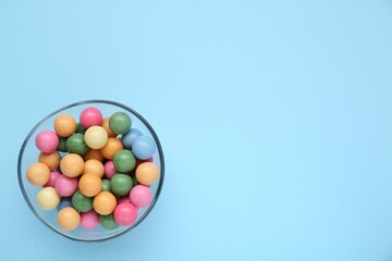 Bowl with many bright gumballs on light blue background, top view. Space for text
