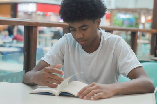 Black Teen Boy In White Shirt With Black Power Hair Reading Umnlivro,various Facial Expressions And Gestures,smiles,copy Space Left