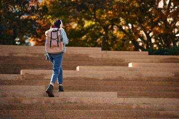 Rear view of woman with backpack and headphones walking up stairs outdoors.