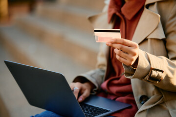 Close up of woman online banking with laptop and credit card outdoors.