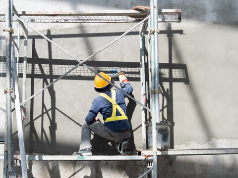 Construction worker plastering concrete wall at a construction site. Working at high scaffolding, safety PPE in construction.