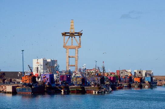 Busy fishing harbor with colorful boats and historic Spanish cable car structure in Sidi Ifni Morocco coastal industry and maritime economy concept