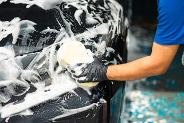 Man worker washing car service with foam and sponge. Car wash cleaning wipe station. Employees clean a vehicle professionally.