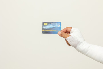 Closeup man broken arm holding credit card payment. Man put on plaster bandage cast splint. Male patient wearing sling support arm after accident injury. Financial life insurance and accident