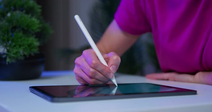 Advertising agency employee is sitting in office at his desk preparing presentation on tablet, zooming in on image on touch screen, completing design of site. Digital artist draws graphic picture