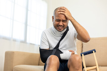 Man suffered pain from accident fracture broken bone injury with leg splints in cast neck splints collar arm splints sling support arm in living room. Social security and health insurance concept.