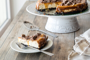 A piece of creamy cheesecake covered in caramel sauce and chocolate chunks.