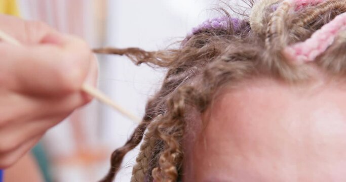  Hairdresser hand unravels the Afro braids carefully pulls out the hair curly whorl. Close-up of a client forehead hairstyle salon correction hairstyles. Unweaving pigtails removal care