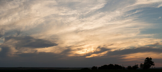Obraz premium A landscape with an enchanting sunset. Panorama. Tragic gloomy sky. The last flashes of the sun on the storm clouds.