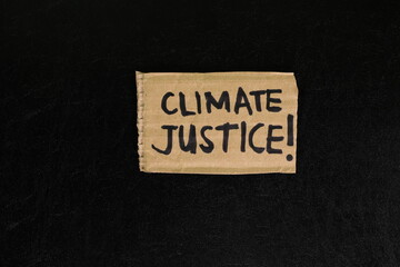 Climate justice concept. Carton placard with handwritten message in dark black background. 