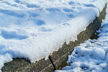 Frosty snow on cement curb in sunlight