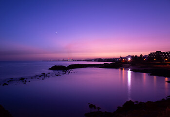 Landscape with lagoon of Playa del Jablillo beach at sunset,. Waxing crescent moon, volcanic rocks, beautiful and colourful view. Romantic vacations in Costa Teguise, Lanzarote. Canary Islands, Spain.